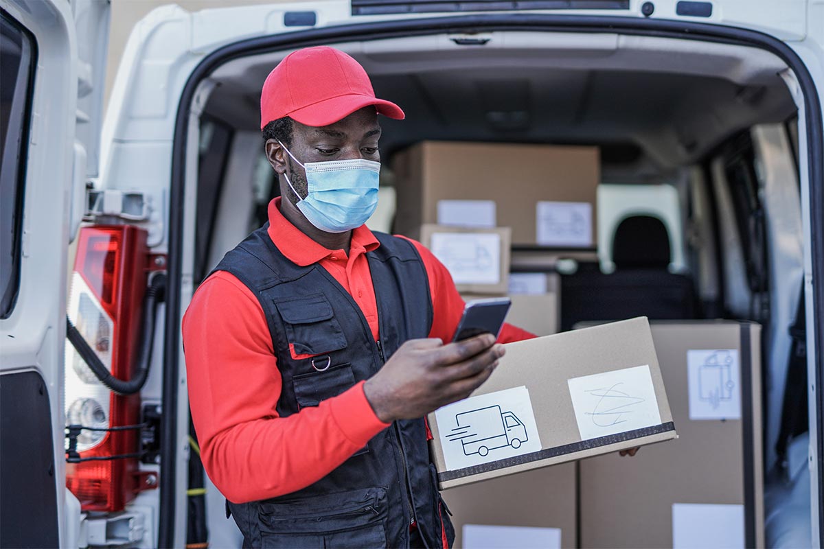 Male delivery guy holding a package while looking at his smartphone